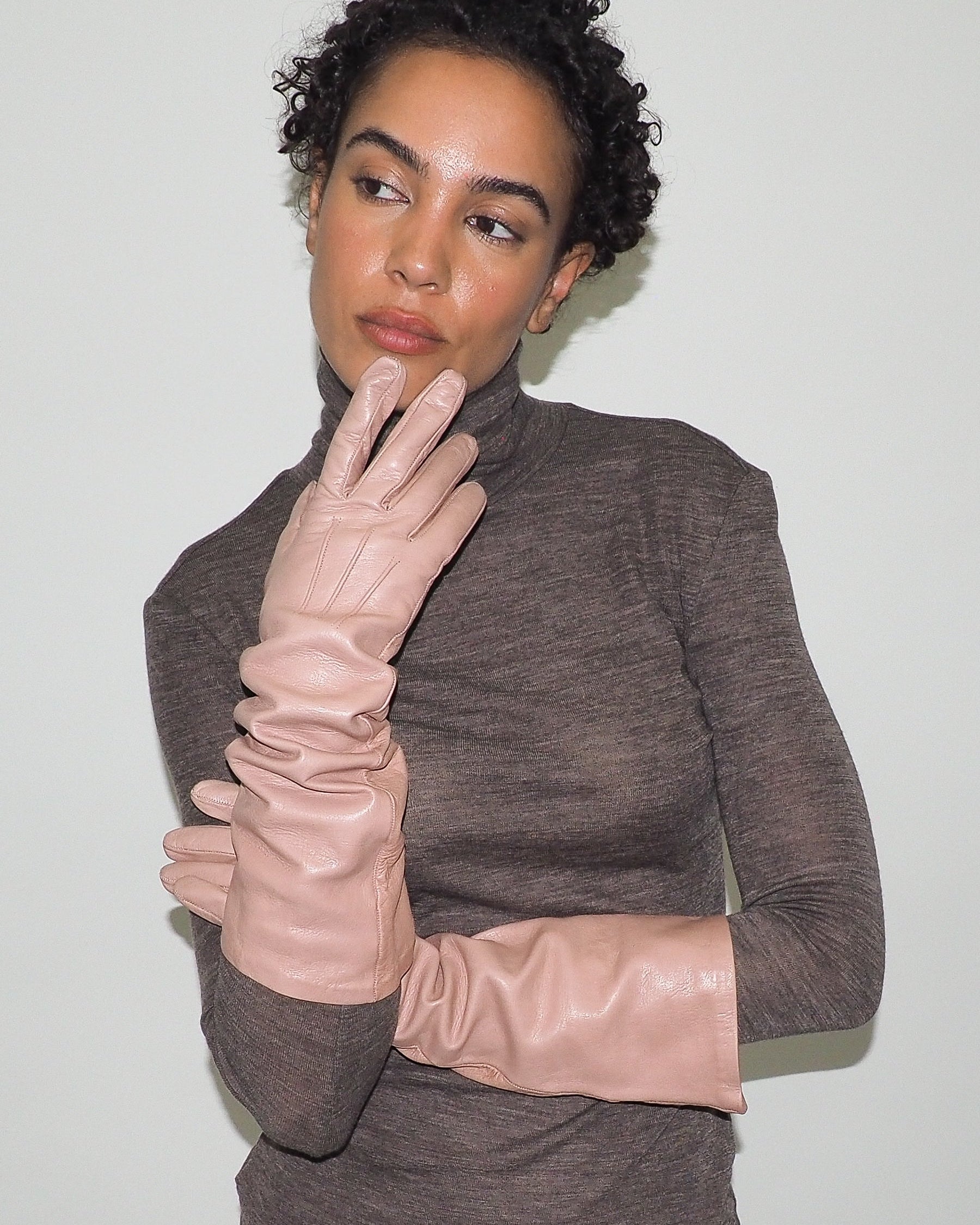 Woman wearing a brown turtleneck sweater and beige gloves against a white background
