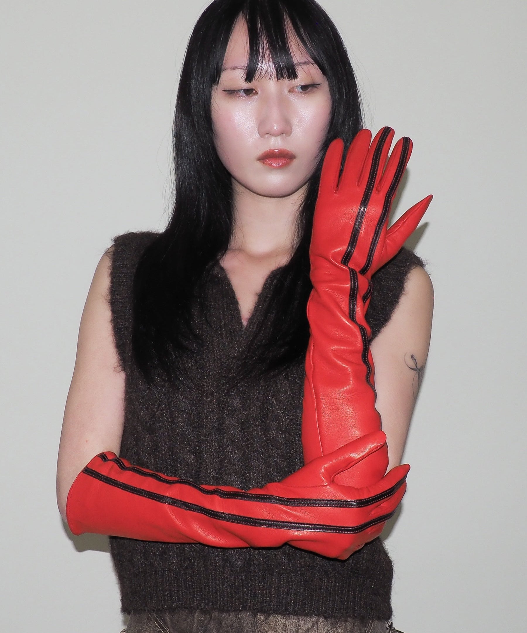 Person wearing a dark sleeveless top and red gloves with black stripes against a plain background