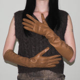 Person wearing a dark brown sleeveless top and brown leather gloves against a plain background