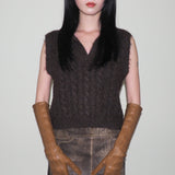 Person wearing a dark brown sleeveless knitted top and brown leather gloves against a plain background