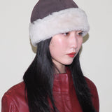 Person wearing a brown hat with white fur trim against a plain background