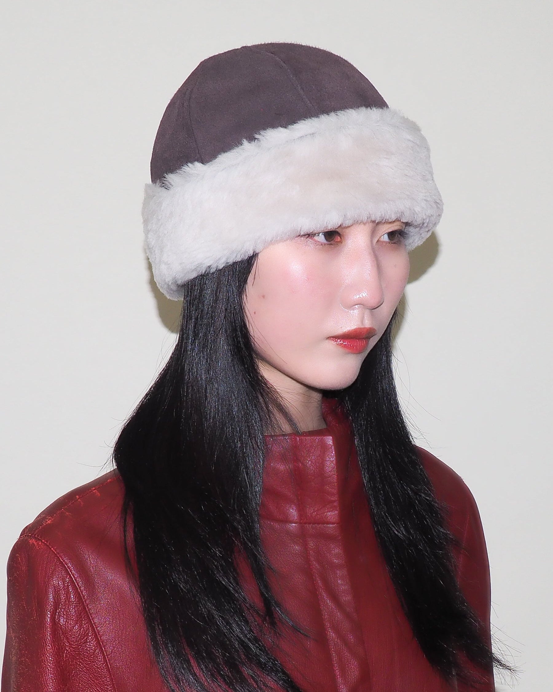 Person wearing a brown hat with white fur trim against a plain background