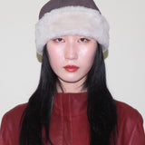 Person wearing a brown hat with white fur trim and a red leather outfit against a plain background