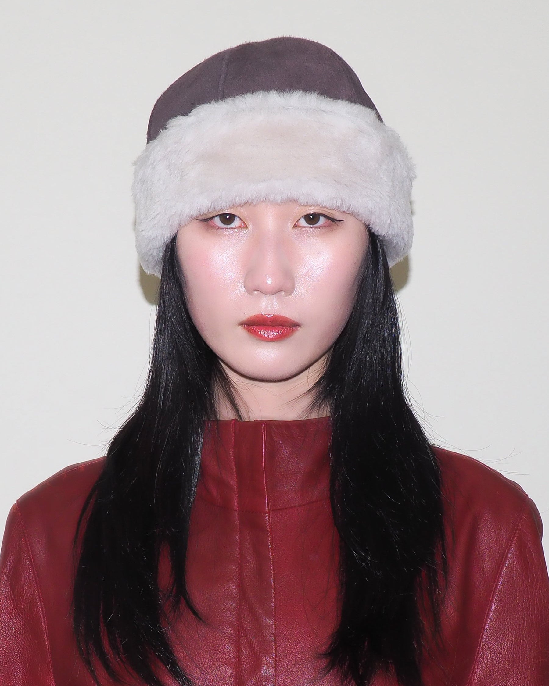Person wearing a brown hat with white fur trim and a red leather outfit against a plain background