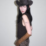 Person wearing a cowboy hat and brown leather gloves against a plain background