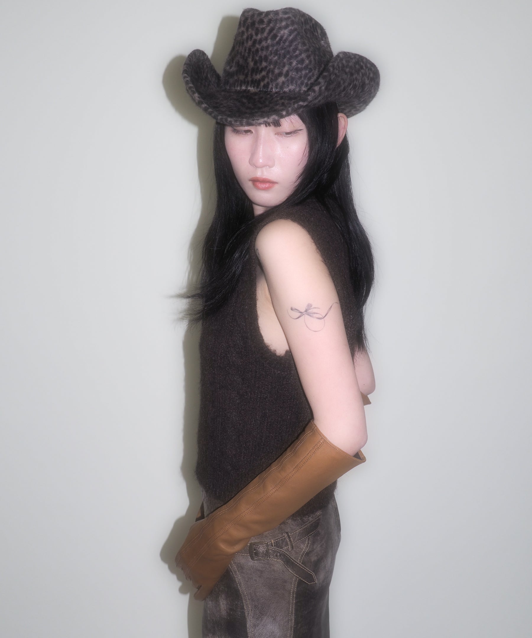 Person wearing a cowboy hat and brown leather gloves against a plain background