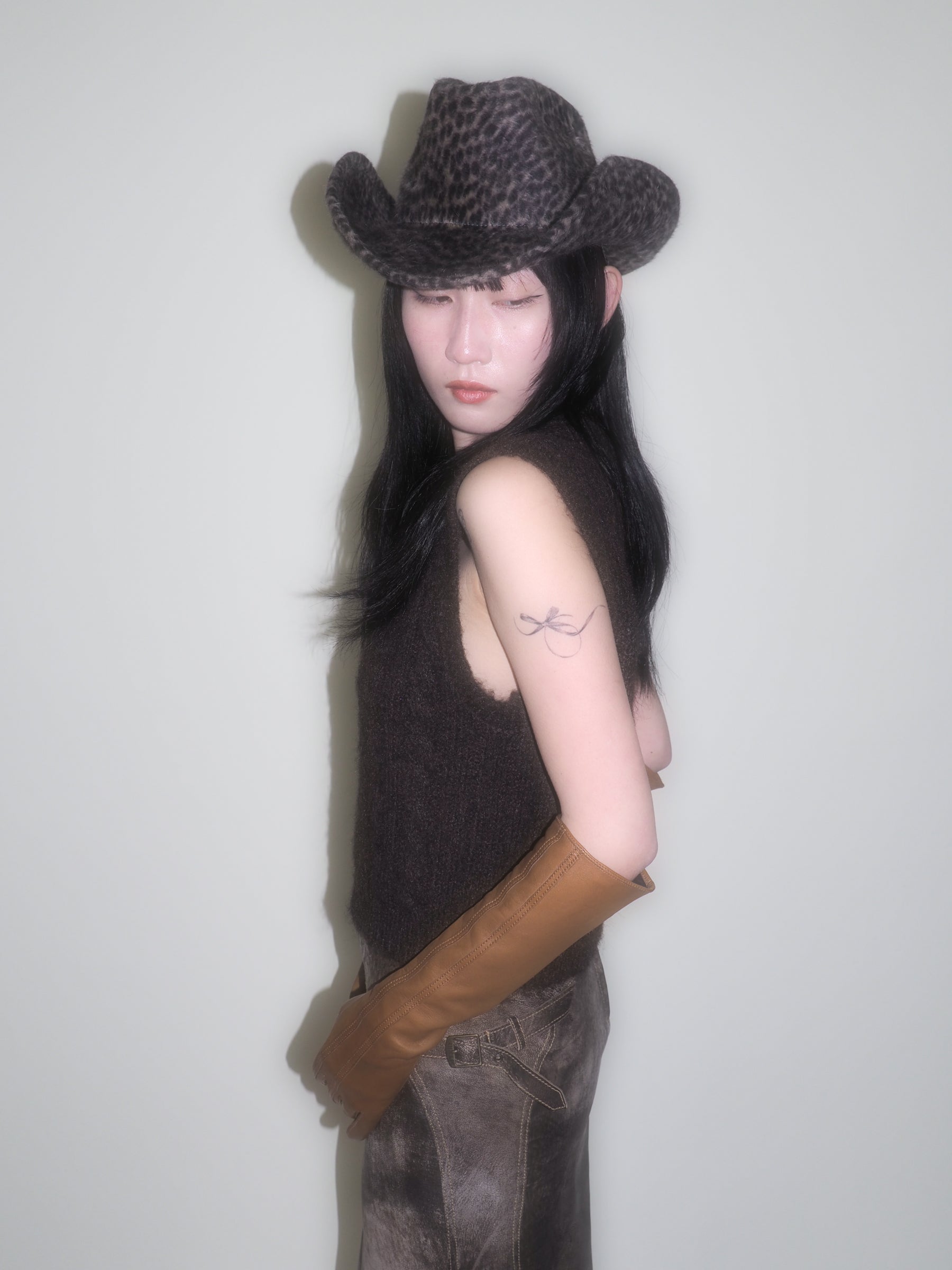 Person wearing a cowboy hat and brown leather gloves against a plain background