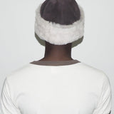 Person wearing a white headband with gray fur trim on a plain background