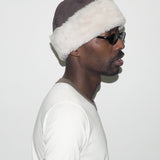 Man wearing a fur-lined hat and sunglasses on a plain background