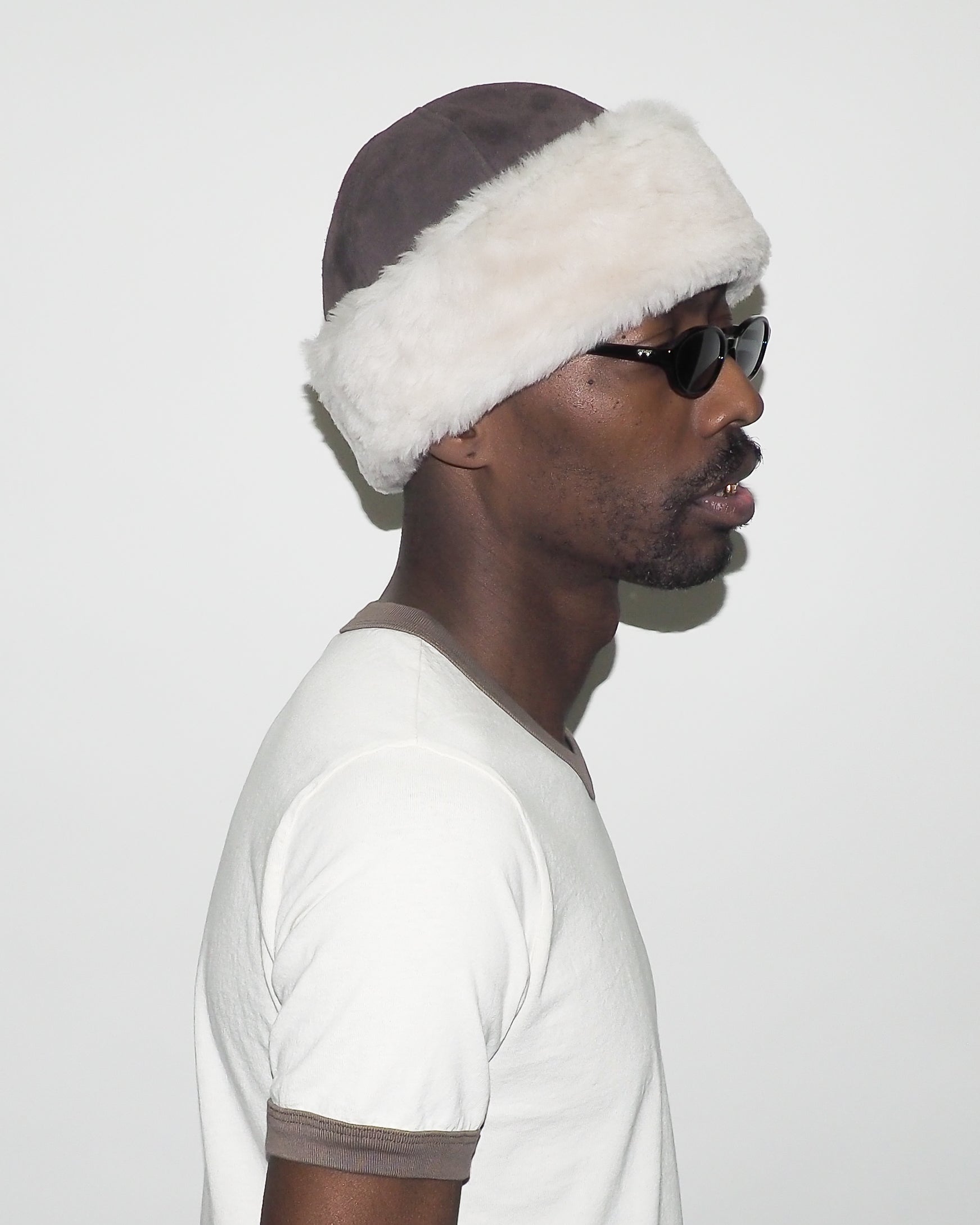 Man wearing a fur-lined hat and sunglasses on a plain background