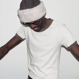 Person wearing a white t-shirt, dark hat with white fur trim, and sunglasses on a plain background