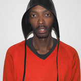 Person wearing a red sweater and black hooded cap against a plain background