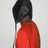 Person wearing a black leather hood with drawstrings on a plain background