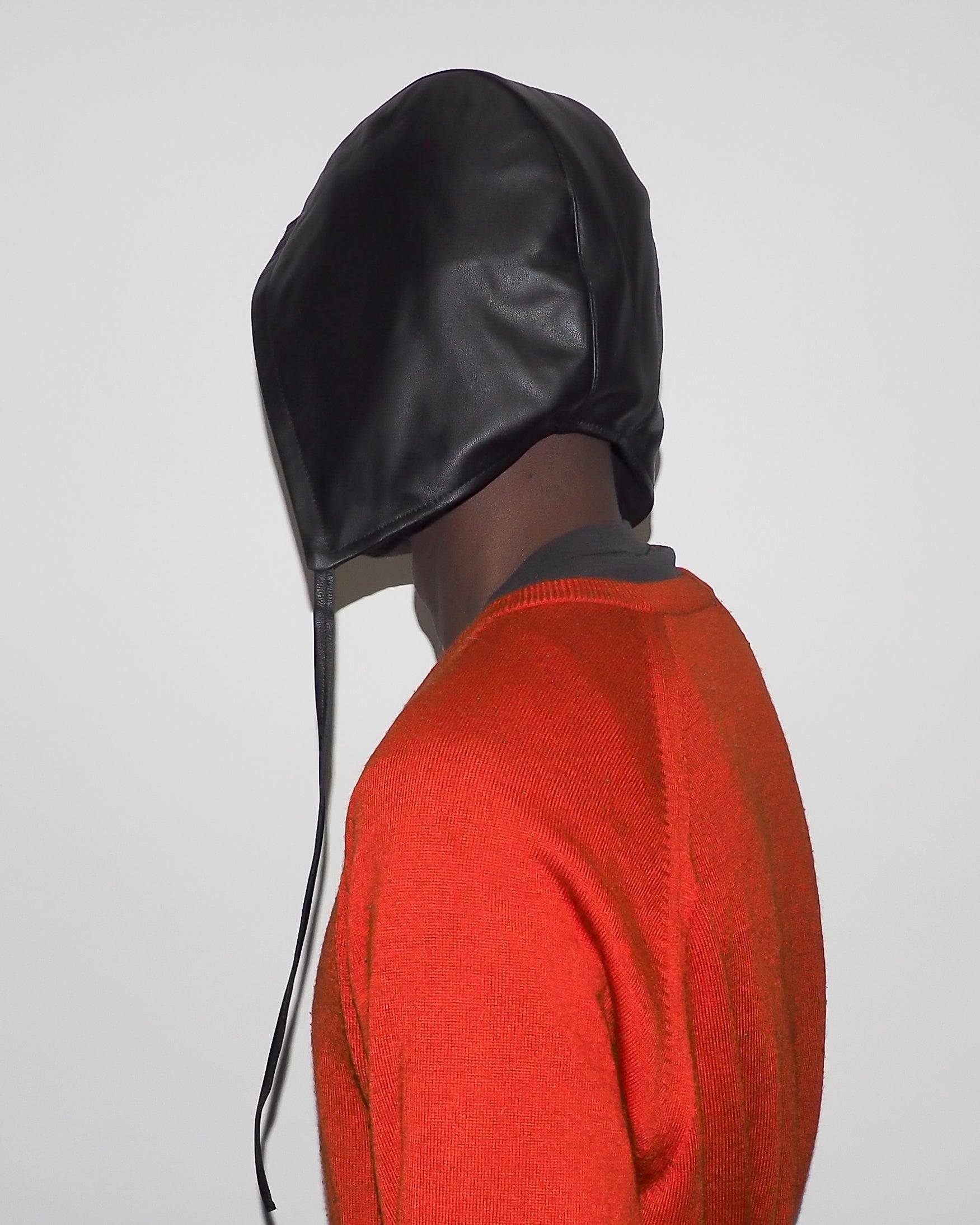 Person wearing a black leather hood with drawstrings on a plain background