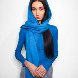 A model wearing a bright blue hooded sweatshirt and matching scarf, paired with a blue, white, and black checkered skirt, standing against a plain white background.