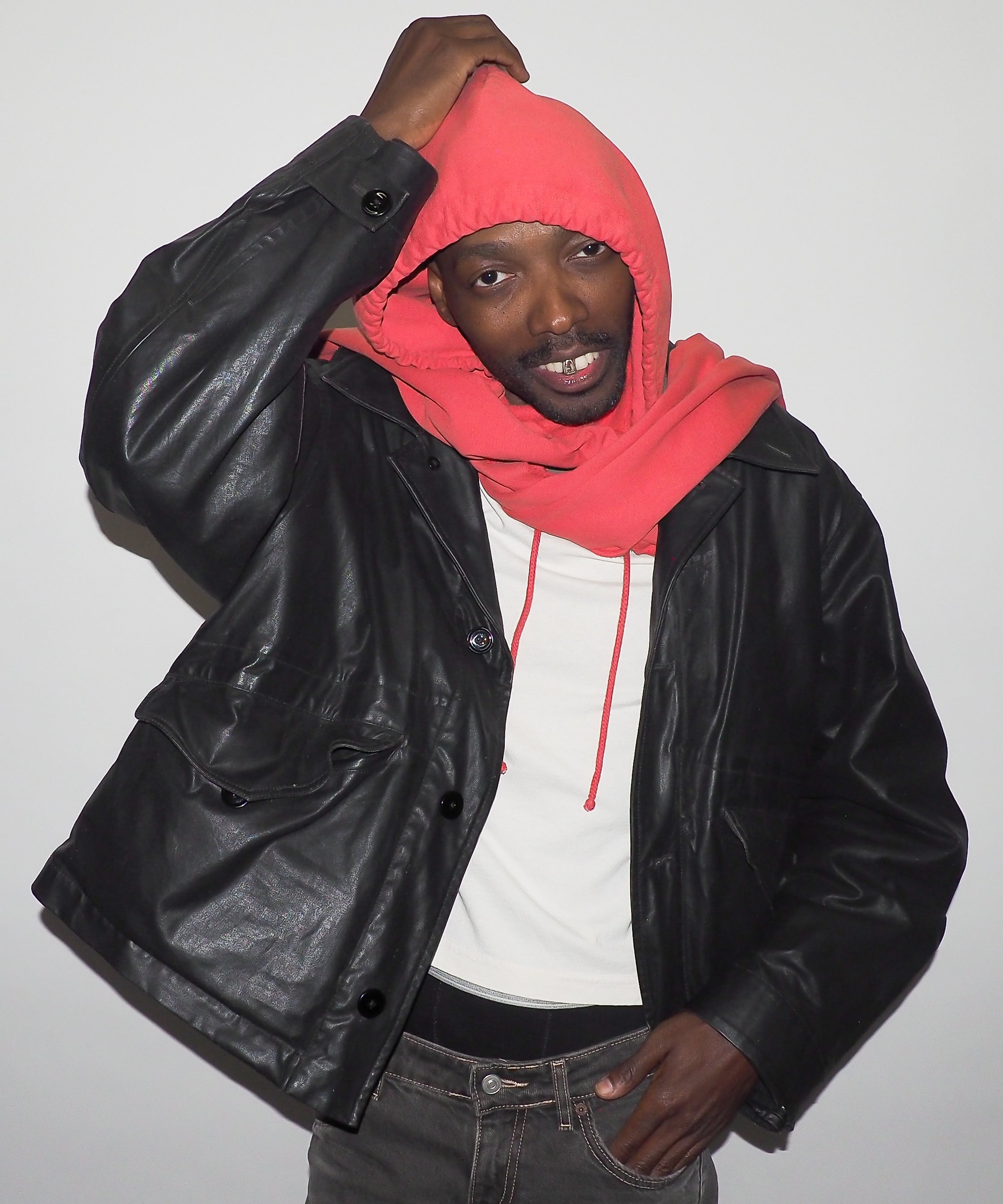 Person wearing a black leather jacket, white shirt, and red hoodie against a plain background