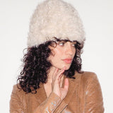 Woman wearing a beige coat and white fur hat on a plain background
