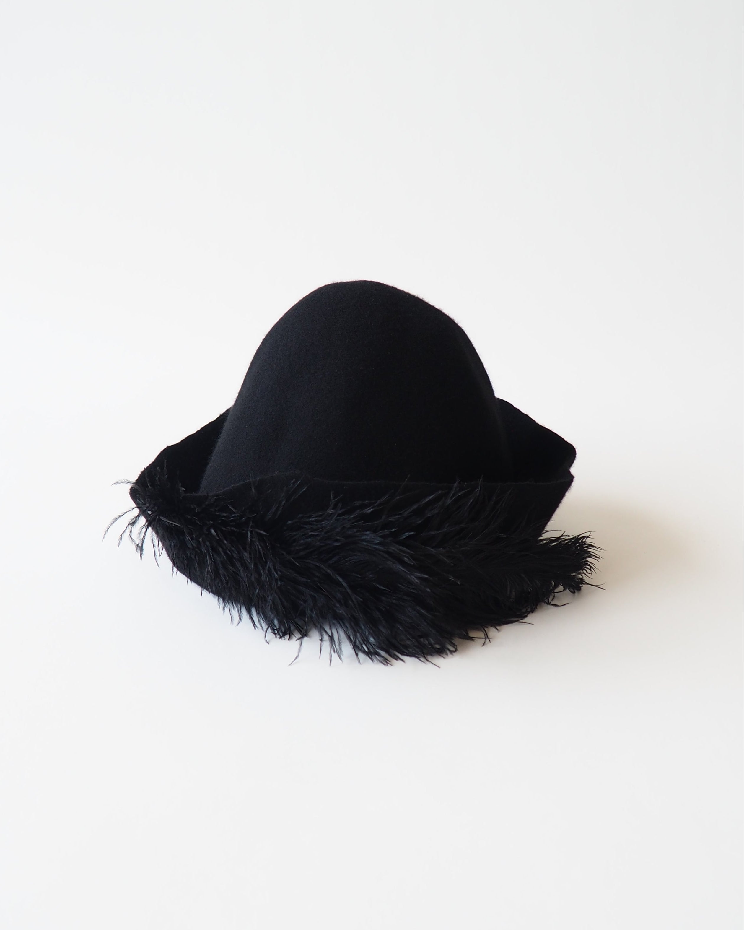 A black cloche hat with a wide brim trimmed in black feathers, photographed on a clean white background.