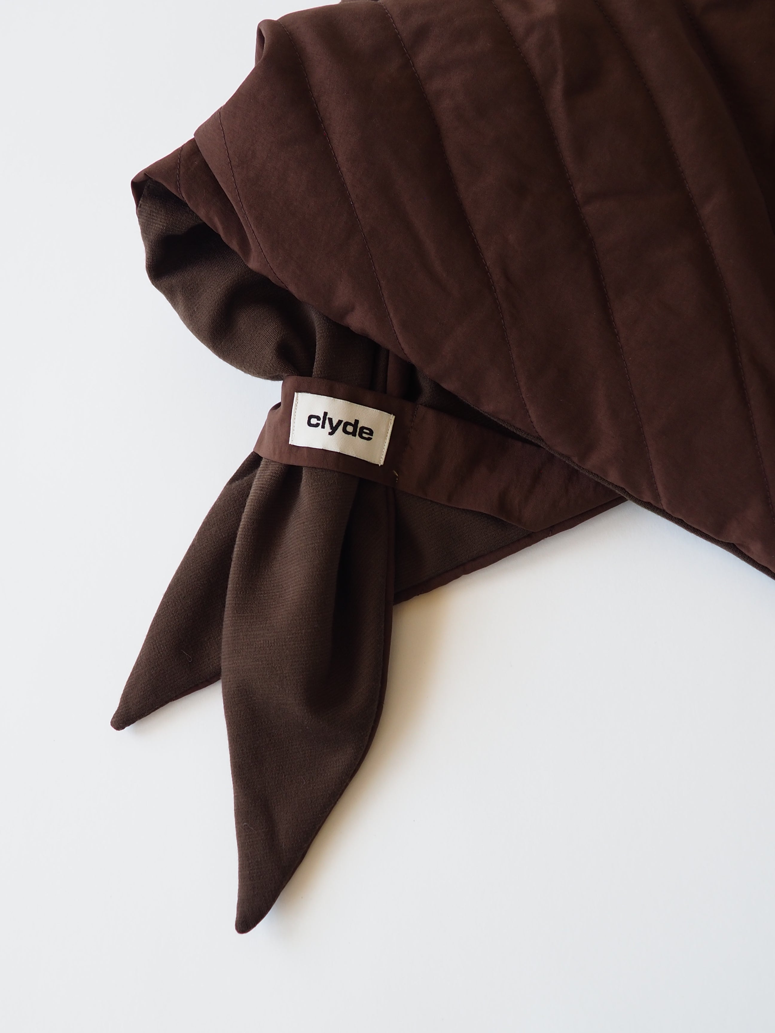 A close-up of a folded dark brown scarf with a small white brand tag reading 'clyde' attached near the corner, set against a plain white background.