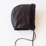 A dark brown faux-leather bonnet with a fuzzy brown trim and long drawstrings, photographed flat on a white background.