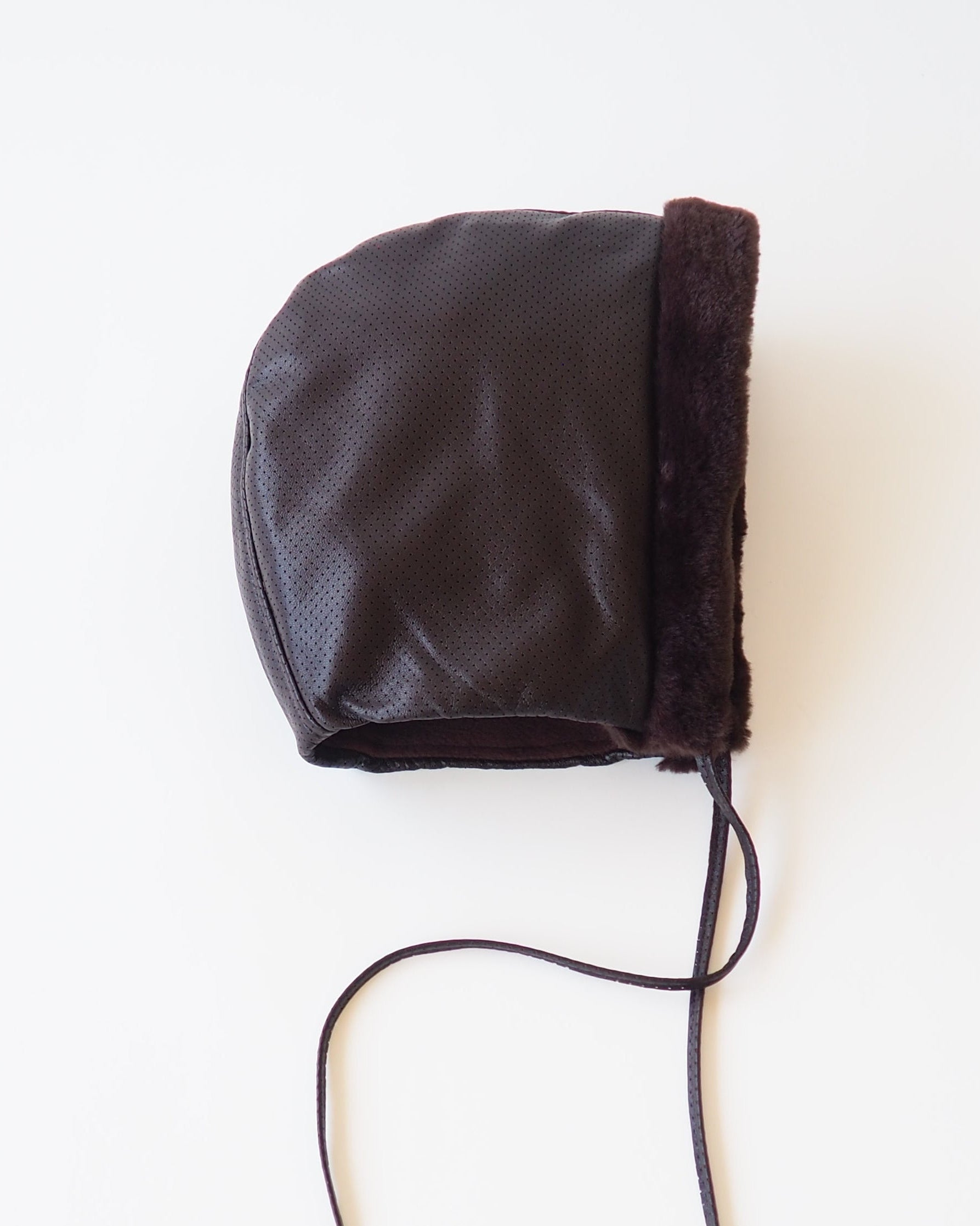 A dark brown faux-leather bonnet with a fuzzy brown trim and long drawstrings, photographed flat on a white background.