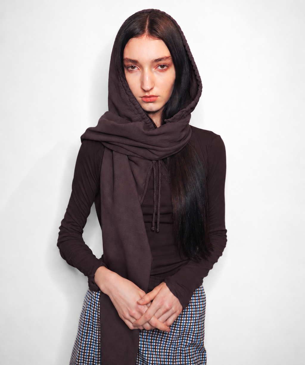 A model wearing a dark brown hooded long-sleeve top and a matching brown scarf, paired with a blue and white checkered skirt, against a plain light gray background.