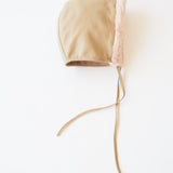 A beige leather bonnet with a light pink faux-fur trim and long beige drawstrings, photographed on a clean white background.